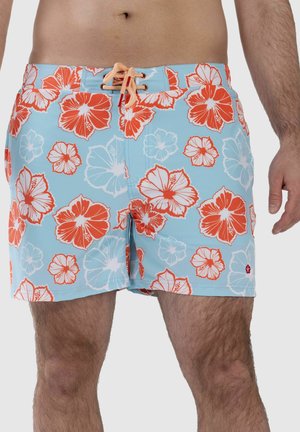 Mann trägt hellblaue Badeshorts mit orange-weißem Hibiskusblumenmuster und pfirsichfarbenem Kordelzug am Bund.