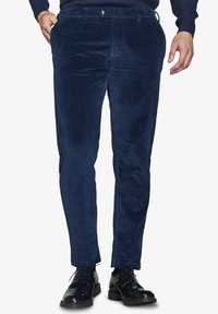 Pantaloni in velluto a coste blu navy con finitura testurizzata, taglio slim, tasche frontali e chiusura con un solo bottone, abbinati a eleganti scarpe da uomo nere lucide.