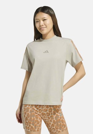 Mujer que lleva una camiseta beige de Adidas con rayas naranjas y pantalones cortos deportivos con estampado de leopardo, de pie con una mano en la cadera.