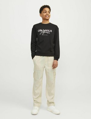 Svart sweatshirt med "ORIGINALS" i vit tryck, beige cargos med sidfickor och vita sneakers. Släta texturer och avslappnad passform.