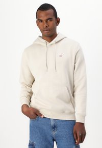 Sudadera con capucha en algodón beige claro, con un bolsillo delantero y un pequeño logo en el pecho. Puños y dobladillo de canalé. Corte casual.