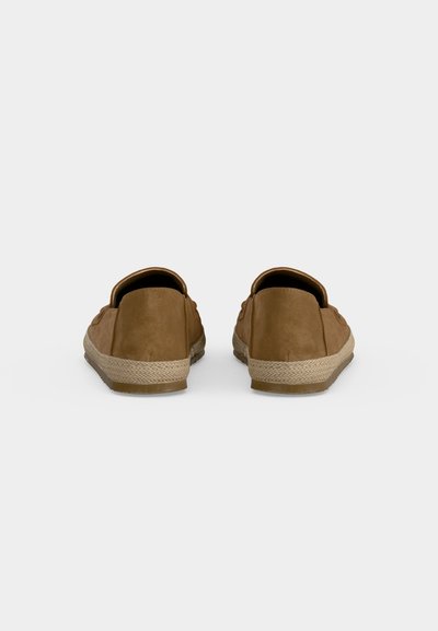 Ζευγάρι καφέ παπούτσια τύπου slip-on με πλεκτό κορδόνι στην καουτσούκ σόλα, εμφανιζόμενα από πίσω σε απλό ανοιχτό φόντο.