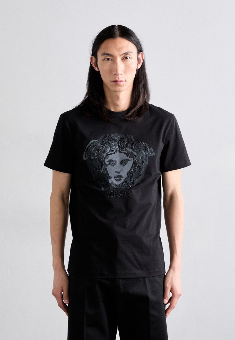 Black cotton t-shirt featuring a Medusa face design with intricate detailing and the "VERSACE" logo below. Short sleeves and round neckline.