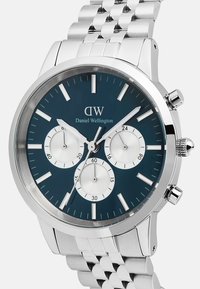 Orologio in acciaio inossidabile con un quadrante rotondo di colore blu navy. Presenta tre sotto-quadranti, indici delle ore in argento e un bracciale a maglie in metallo.