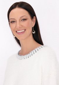 Pulover alb pufos cu decolteu cu dungi negre. Modelul poartă cercei aurii cu accente circulare și două perle, zâmbind.