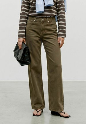 Personne portant un pantalon large vert olive, un chemisier rayé à manches longues, des sandales compensées noires, tenant une pochette noire.