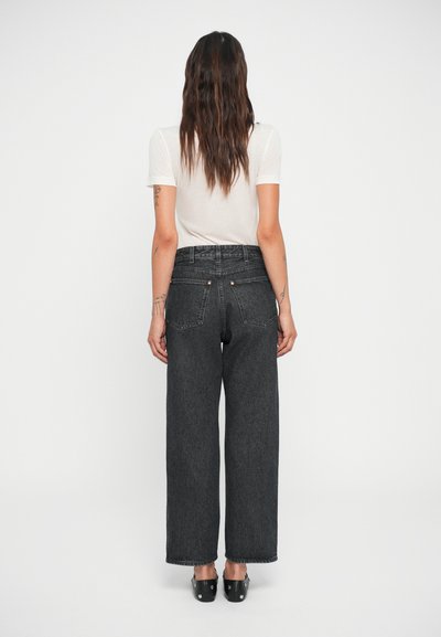 Hoge taille zwarte denim jeans met een ruime pasvorm, subtiele textuur, achterzakken en zilveren hardware accenten. Draagt met een aansluitend licht shirt.