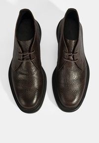 Bruine leren schoenen met een gestructureerd oppervlak, ronde neus en dunne veters. Beschikt over een zwarte rubberen zool en geen zichtbare naden.