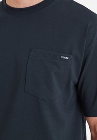 Dark navy cotton t-shirt with a crew neckline, short sleeves, and a chest pocket. Features a small white "TOG24" label on the pocket.