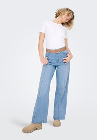 Ljusblå jeans med vida ben och framåtsydd söm, kombinerat med en vit figursydd t-shirt och ett tanfärgat skärp, kompletterat med beige skor med grov sula.