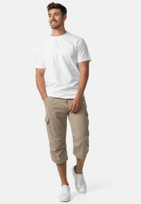 Biała bawełniana koszulka zestawiona z jasnobeżowymi szortami cargo z bocznymi kieszeniami. Model nosi białe sneakersy. Prosty, casualowy styl.