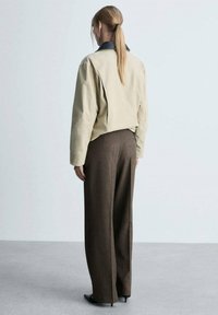 Veste cropped beige avec col noir, associée à un pantalon large marron. Tissu lisse avec un design structuré et un minimalisme dans les détails.