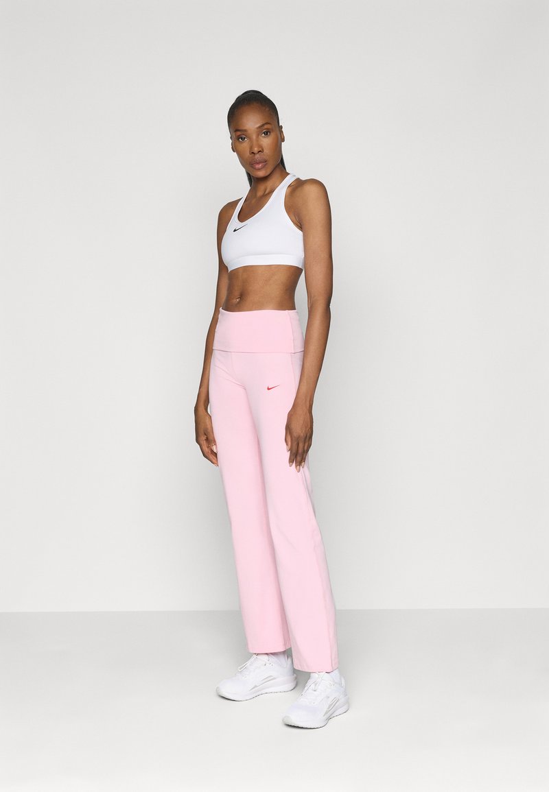 Brassiere sportivo bianco con logo Nike nero, abbinato a pantaloni alti leggeri rosa con un piccolo logo Nike rosso. Scarpe da atletica bianche.