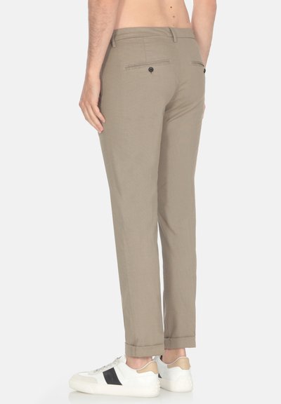 Pantaloni beige con una vestibilità affusolata, tasche laterali e due tasche posteriori, dotati di chiusure a bottone e una texture liscia, abbinati a sneakers bianche.