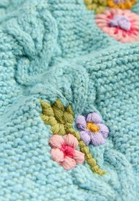 Tessuto lavorato a maglia blu chiaro con ricami floreali in rosa, lavanda e giallo, arricchito da dettagli a rilievo a trecce.