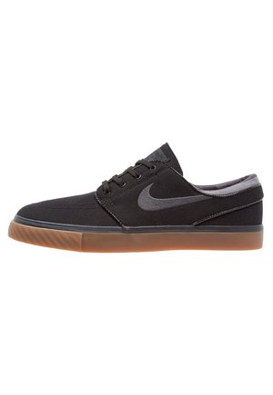 Zapatilla Nike baja negra con suela de goma marrón, cordones negros y logo Nike swoosh gris en el lateral.