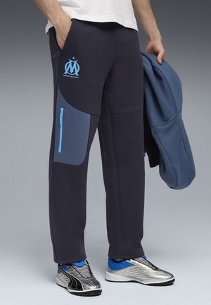 Mørkeblå sweatpants med lyseblå detaljer, der har en lynlås-lomme, logo på låret og en afslappet pasform. Bæres med en matchende jakke.