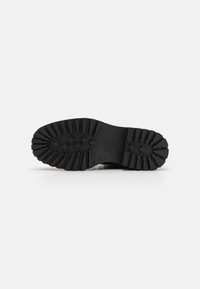 Semelle en caoutchouc noir avec des crampons profonds, comprenant des rainures et des motifs croisés pour une adhérence optimale. Design robuste et plat adapté à diverses surfaces.