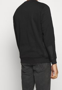 Svart sweatshirt med rund halsringning, långa ärmar och ribbade ärmslut. Har en texturerad sidopanel och ett mjukt, slätt tyg.