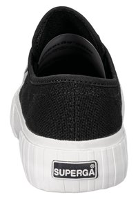 Sneaker nera in tela con suola in gomma bianca, forma arrotondata e una toppa posteriore che mostra il logo "SUPERGA". Tessuto dalla texture visibile.