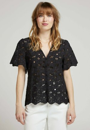 Blouse en dentelle noire avec découpes florales, décolleté en V et manches volantées, dotée d'un ourlet à bords festonnés et d'une texture légère.
