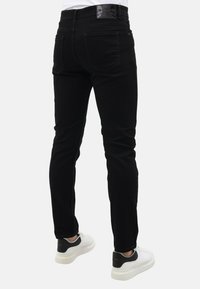 Zwarte spijkerbroek van denim met een strakke pasvorm, voorzien van achterzakken, riemlussen en een label op de tailleband. Gecombineerd met witte en grijze sneakers.