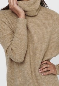Maglione beige a collo alto con un motivo di maglia testurizzato, caratterizzato da maniche lunghe e una vestibilità rilassata, mostrato su uno sfondo neutro.