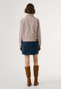 Giacca in tessuto rigato con colletto, abbinata a una mini gonna di jeans. La modella indossa stivali di camoscio marroni fino al ginocchio. Vista posteriore.