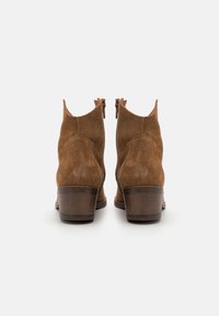 Botas de ante marrón hasta el tobillo con un tacón de altura media, que presentan una punta redonda, cremalleras laterales y un detalle texturizado en el tacón.