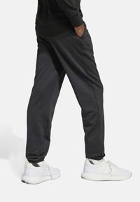 Donkergrijze broek met taps toelopende benen, zijzakken en ribbels aan de manchetten, gecombineerd met witte sneakers met een gestructureerde bovenkant en een gevoerde zool.