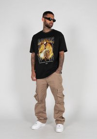 Sort grafisk t-shirt med et skeletdesign og gule detaljer, parret med cargo-bukser. Hvide sneakers fuldender outfittet.