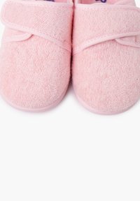 Zapatillas suaves de tela rosa claro con superficie texturizada, que cuentan con una correa de Velcro en la parte superior y una suela de goma para mayor agarre.