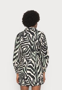 Vestido de manga longa com padrão de zebra em preto, branco e verde; possui um decote com colarinho e punhos elásticos. Textura do tecido suave.