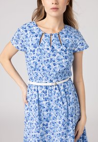 Il vestito floreale presenta un motivo blu chiaro, un collo rotondo con aperture a forma di chiave, maniche corte e una cintura bianca in vita.