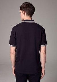 Fekete póló klasszikus dizájnnal, három gombos nyakkal és kontrasztos fehér csíkokkal a galléron és az ujjakon.