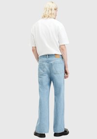 Jeans de mezclilla de color azul claro con un corte holgado, cuentan con bolsillos traseros y una etiqueta de cuero marrón en la cintura. Combinados con una camiseta blanca sencilla.