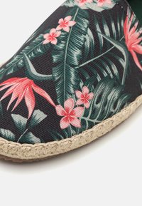 Espadrille with a black fabric upper featuring tropical floral patterns in pink and green. Jute rope sole adds texture and contrast.