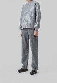 Veste bomber argentée avec une finition brillante, col et poignets côtelés. Assortie à un pantalon large à rayures grises et des chaussures noires robustes.