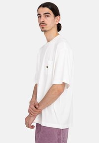 White cotton t-shirt with short sleeves, a relaxed fit, and a left chest pocket featuring a multicolored embroidered design.