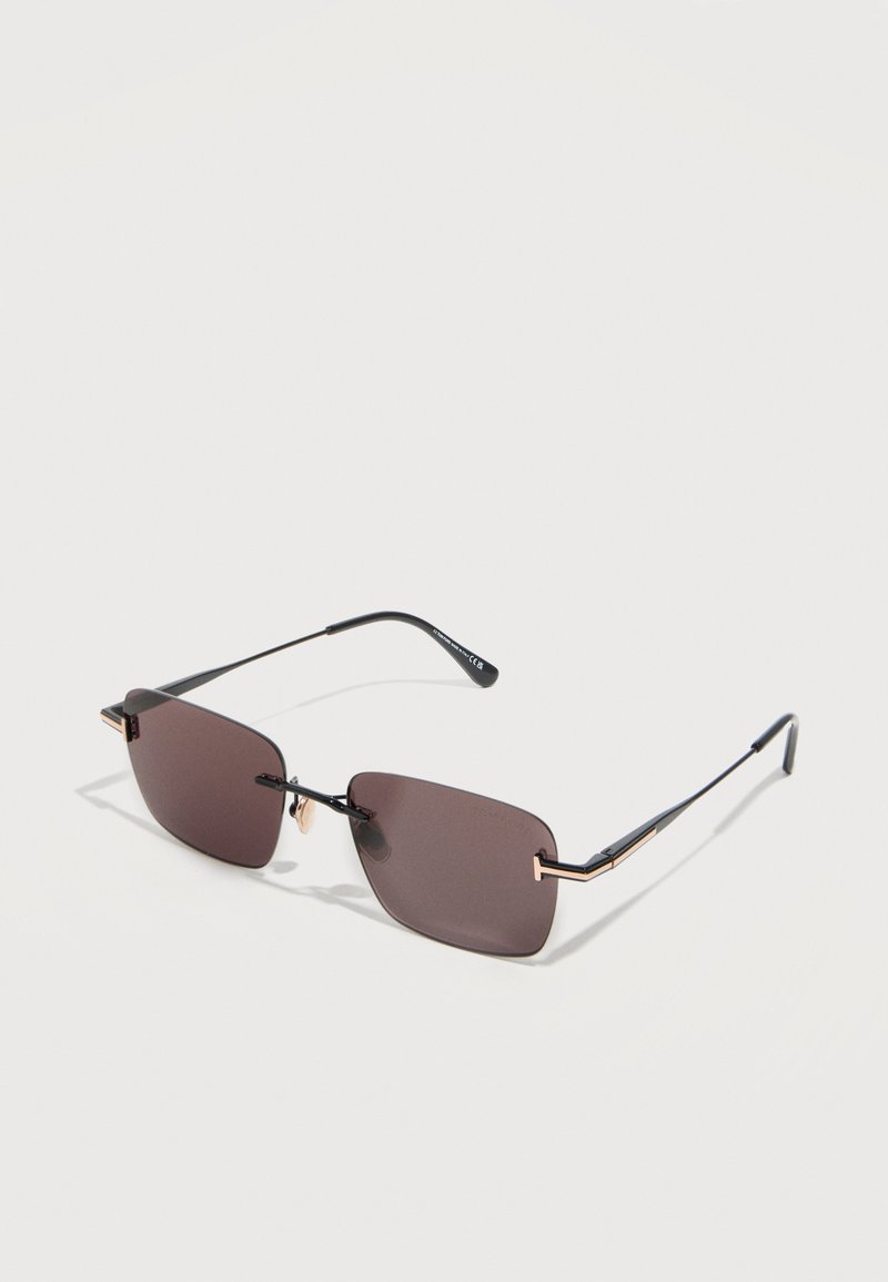 Rectangular rimless sunglasses with dark brown lenses and thin black metal temples featuring gold accents on a light background.