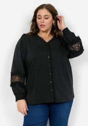 Zwarte blouse met een V-hals, knoopsluiting en getextureerde kantaccenten op de mouwen. Zacht materiaal, ruime pasvorm en gerimpelde manchetten.