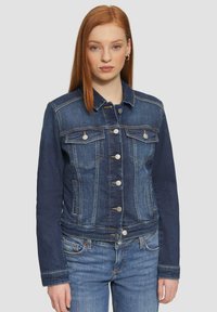 Donkerblauwe denimjack met een knopenlijst aan de voorkant, twee borstzakken en contrasterende stiksels. Heeft lange mouwen en een getailleerd ontwerp.