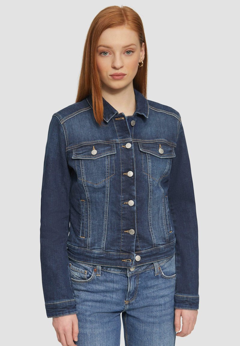 Donkerblauwe denimjack met een knopenlijst aan de voorkant, twee borstzakken en contrasterende stiksels. Heeft lange mouwen en een getailleerd ontwerp.