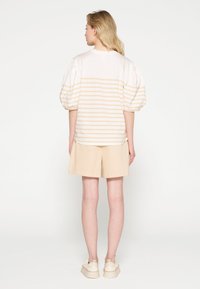 Camisa blanca y beige a rayas con mangas abullonadas, combinada con pantalones cortos beige. La textura es suave; la camisa tiene un cuello redondo y un corte holgado.
