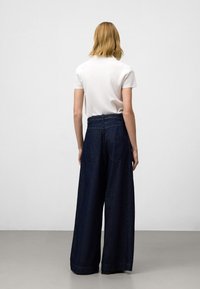 Lättvikts vit polo skjorta i kombination med högmidjade, vida mörkblå denimjeans som har två bakfickor och upprullad fåll.