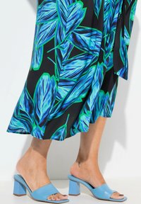 Blå blockklackade sandaler med en bred rem, designade i slät läder. Mönstrad svart kjol med livfulla blå och gröna bladmönster.