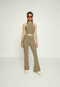 Conjunto de duas peças com riscas, apresentando um top cropped e calças flare em tons de terra. Tecido liso e elástico com um design justo. Sapatos chunky de cor creme.