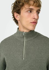 Groene geribbelde gebreide trui met een hoge kraag en een kwartrits. Zachte textuur en aansluitend ontwerp. Minimalistische stijl zonder zichtbare logo's.