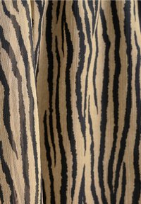 Textil mit einem neutralen beigen Hintergrund und kräftigen schwarzen Tigerstreifen, das eine strukturierte Webart und ein dynamisches Muster zeigt.