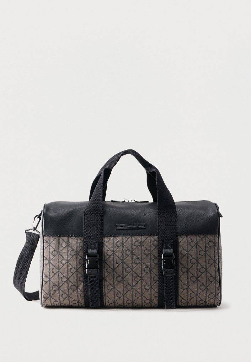 Καφέ ορθογώνια τσάντα duffel με σχέδιο, μαύρο δερμάτινο πάνω μέρος, δύο μαύρες λαβές, ρυθμιζόμενο ιμάντα ώμου και εμπρόσθιους ιμάντες με πόρπη.